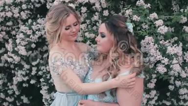 两个姐姐穿着蓝色的llight豪华的奇妙连衣裙在花园里靠近白花。 女人轻轻地纠正